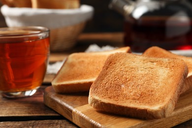 Photo of Slices of tasty toasted bread and aromatic tea n wooden table, closeup