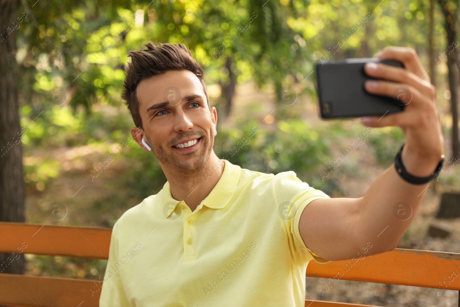 Photo of Young man with wireless earphones taking selfie in park