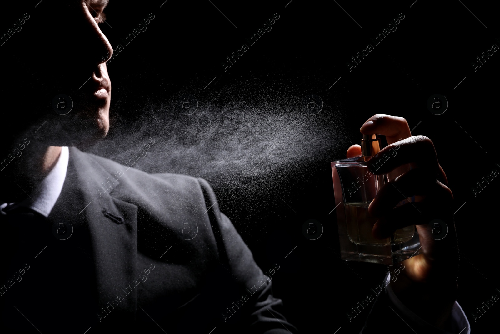 Photo of Man spraying luxury perfume on black background, closeup