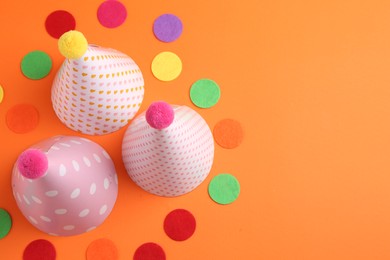 Party hats and colorful confetti on orange background, flat lay. Space for text