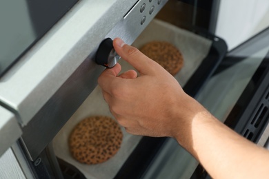 Young man baking cookies in oven at home, closeup