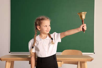 Pupil with school bell near chalkboard in classroom