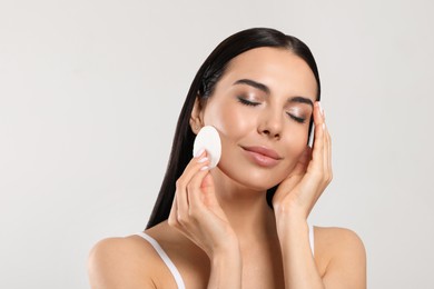 Photo of Young woman using cotton pad with micellar water on light grey background