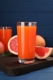 Photo of Tasty grapefruit juice in glass and fresh fruits on blue wooden table