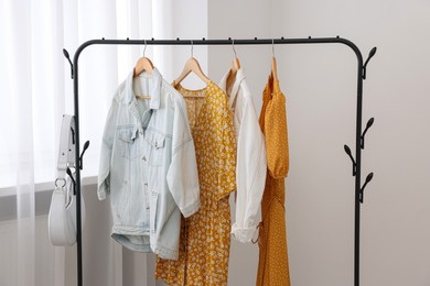 Rack with bag and stylish women's clothes on hangers near light wall indoors