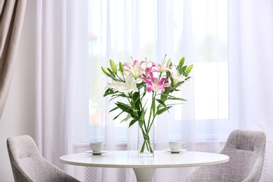 Vase with bouquet of beautiful lilies on white table indoors