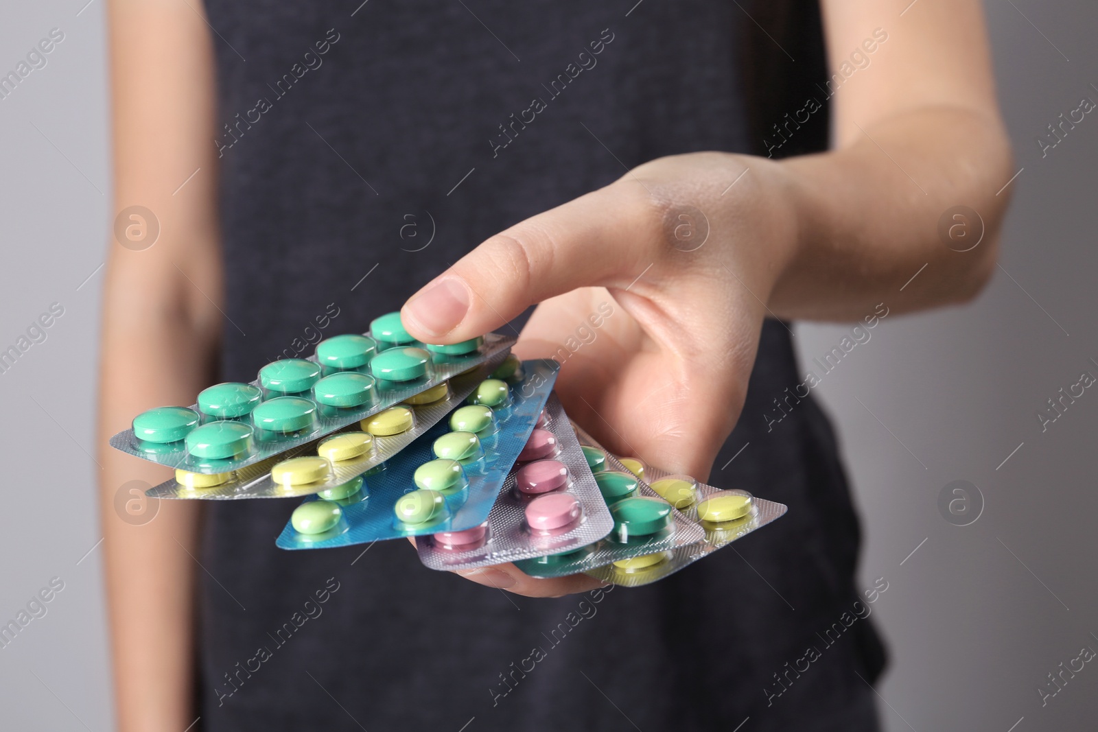 Photo of Woman holding pills in blister packs on gray background, closeup