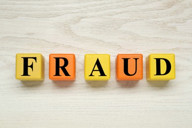 Photo of Word Fraud of cubes with letters on white wooden background, flat lay
