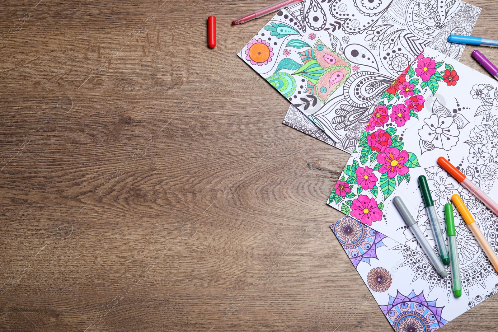 Photo of Antistress coloring pages and felt tip pens on wooden table, flat lay. Space for text