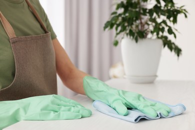 Woman with microfiber cloth cleaning white table in room, closeup