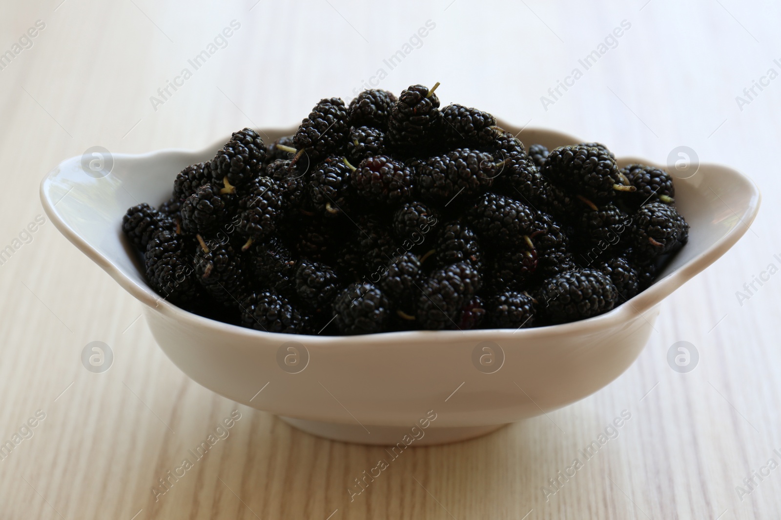 Photo of Bowl of delicious ripe black mulberries on wooden table