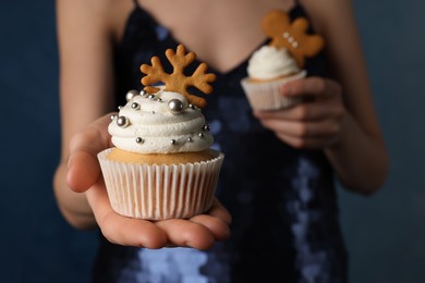 Photo of Woman holding tasty Christmas cupcakes on blue background, closeup