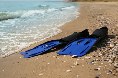 Pair of blue flippers on sand near sea, closeup