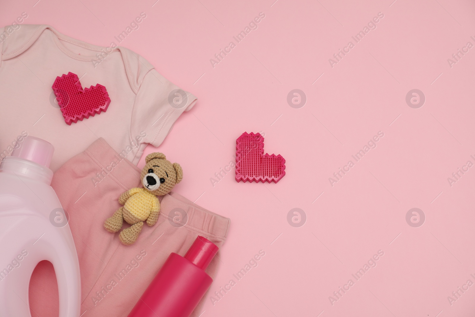 Photo of Bottles of laundry detergents, baby clothes, toy bear and decorative hearts on pink background, flat lay. Space for text