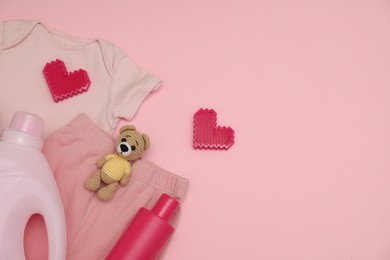 Bottles of laundry detergents, baby clothes, toy bear and decorative hearts on pink background, flat lay. Space for text