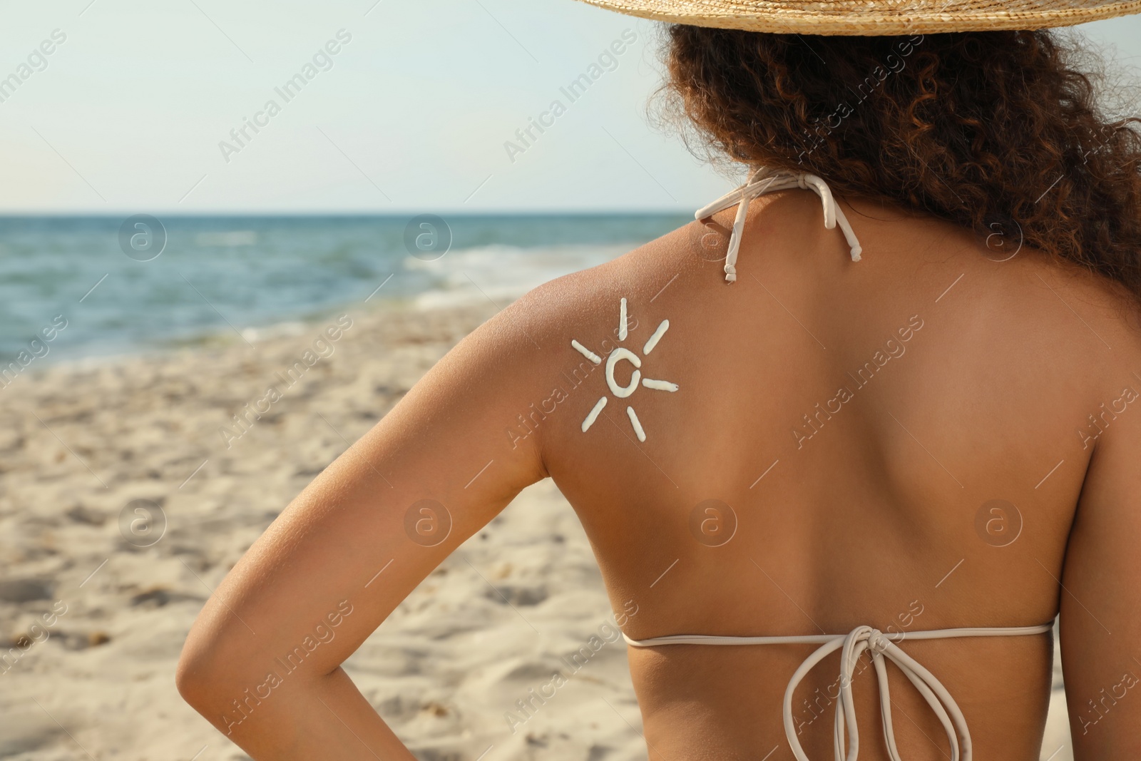 Photo of African American woman with sun protection cream on shoulder at beach, back view