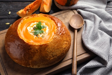 Photo of Tasty pumpkin soup served in bread on table