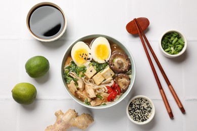 Noodle soup. Bowl of delicious ramen, ingredients and chopsticks on white tiled table, flat lay