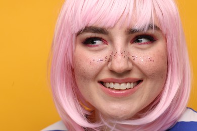 Photo of Smiling woman with bright makeup and glitter freckles on yellow background, closeup