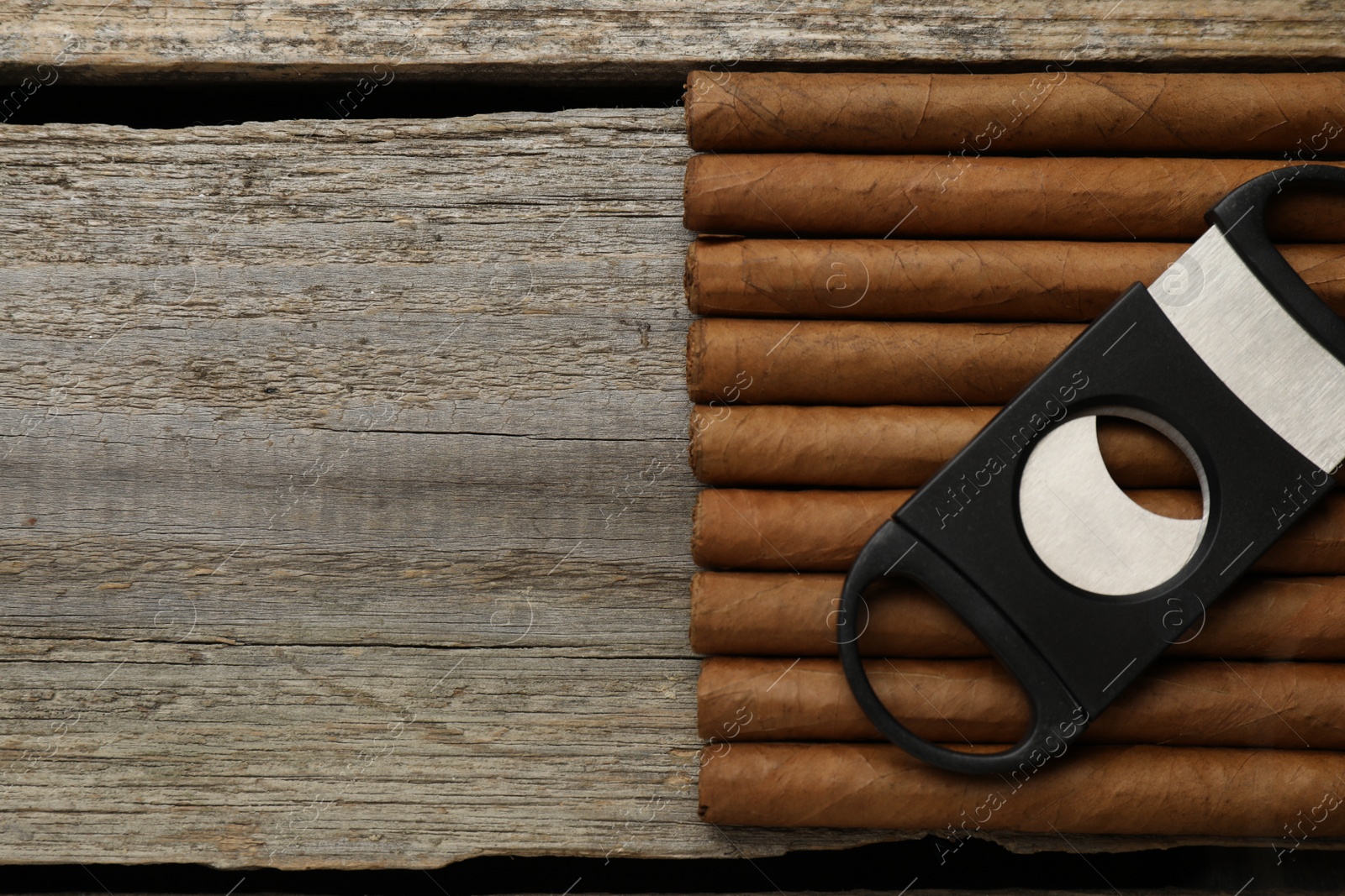 Photo of Cigars and guillotine cutter on wooden table, top view. Space for text