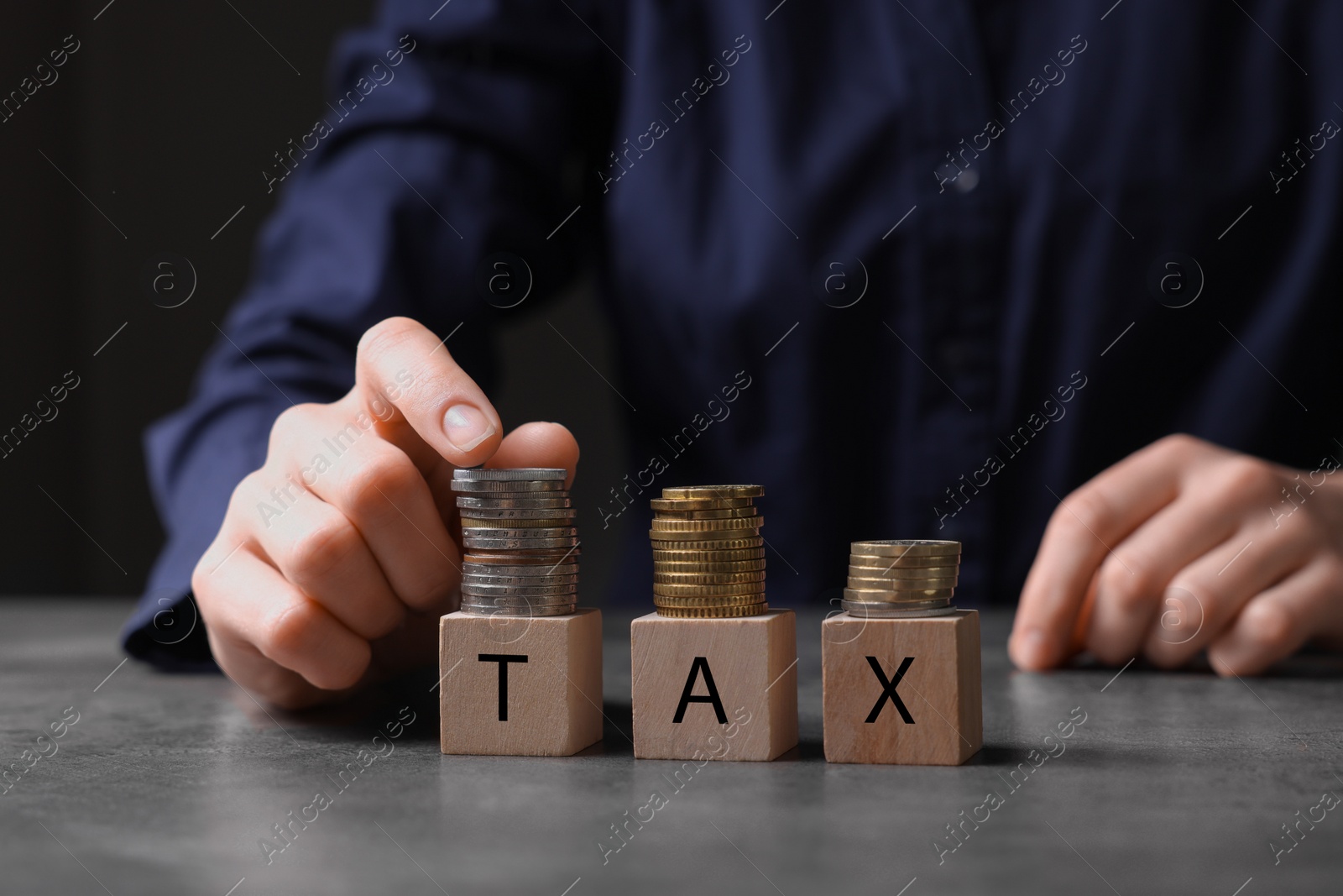 Photo of Woman with word Tax made of wooden cubes and coins at grey table, closeup