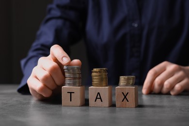 Woman with word Tax made of wooden cubes and coins at grey table, closeup