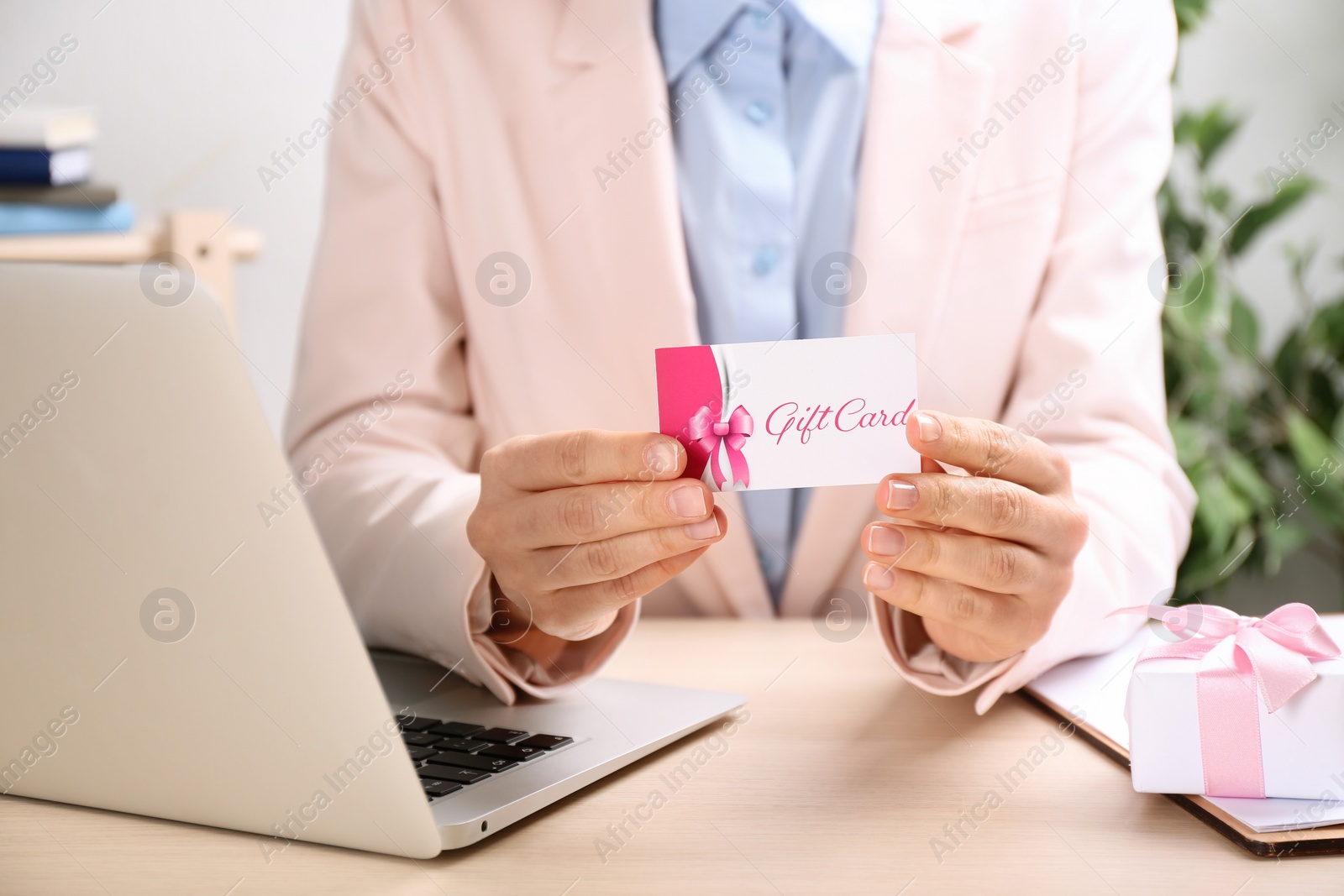 Photo of Woman with gift card and laptop at table indoors, closeup