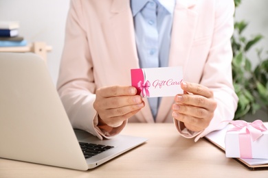 Photo of Woman with gift card and laptop at table indoors, closeup