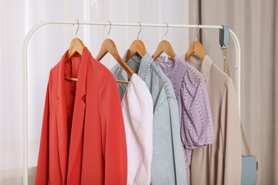 Photo of Clothing rack with stylish women's clothes on wooden hangers indoors