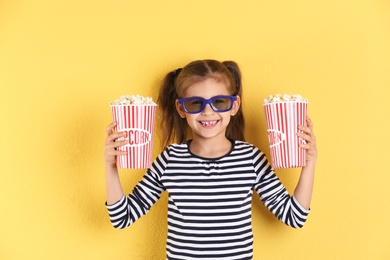 Cute little girl with popcorn and glasses on color background