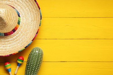 Mexican sombrero hat, maracas and toy cactus on yellow wooden background, flat lay. Space for text