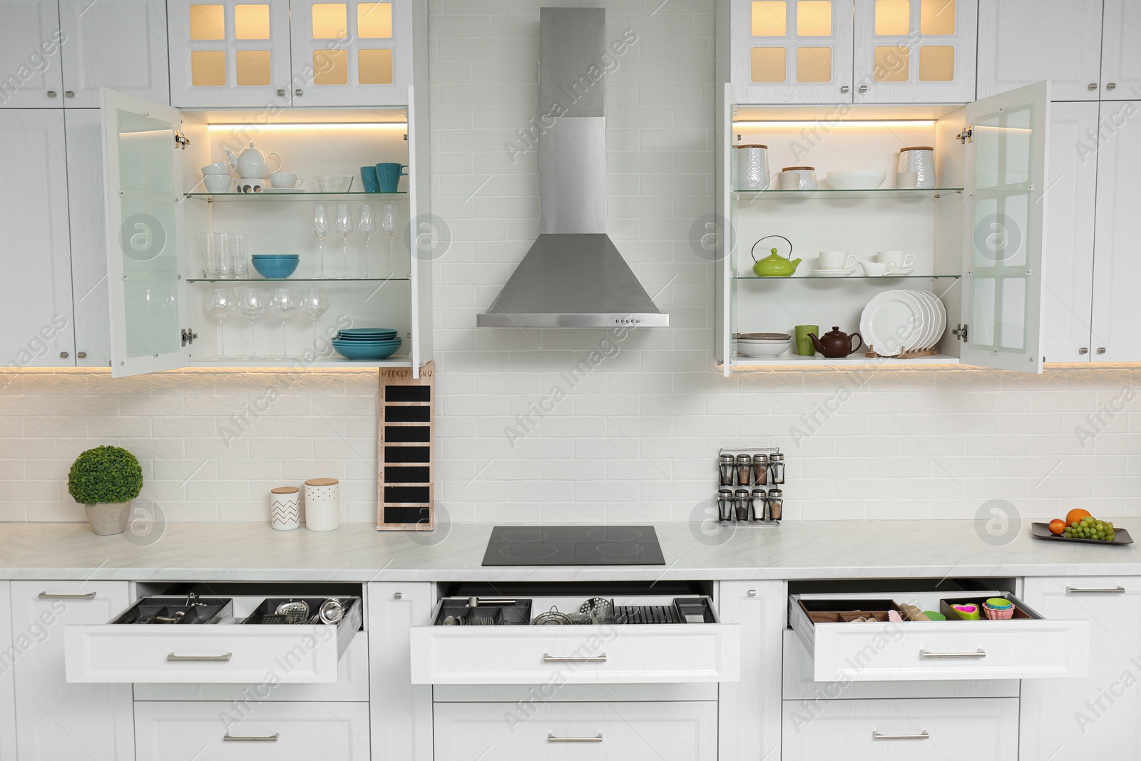 Photo of Open cabinets with different clean tableware and utensils in kitchen