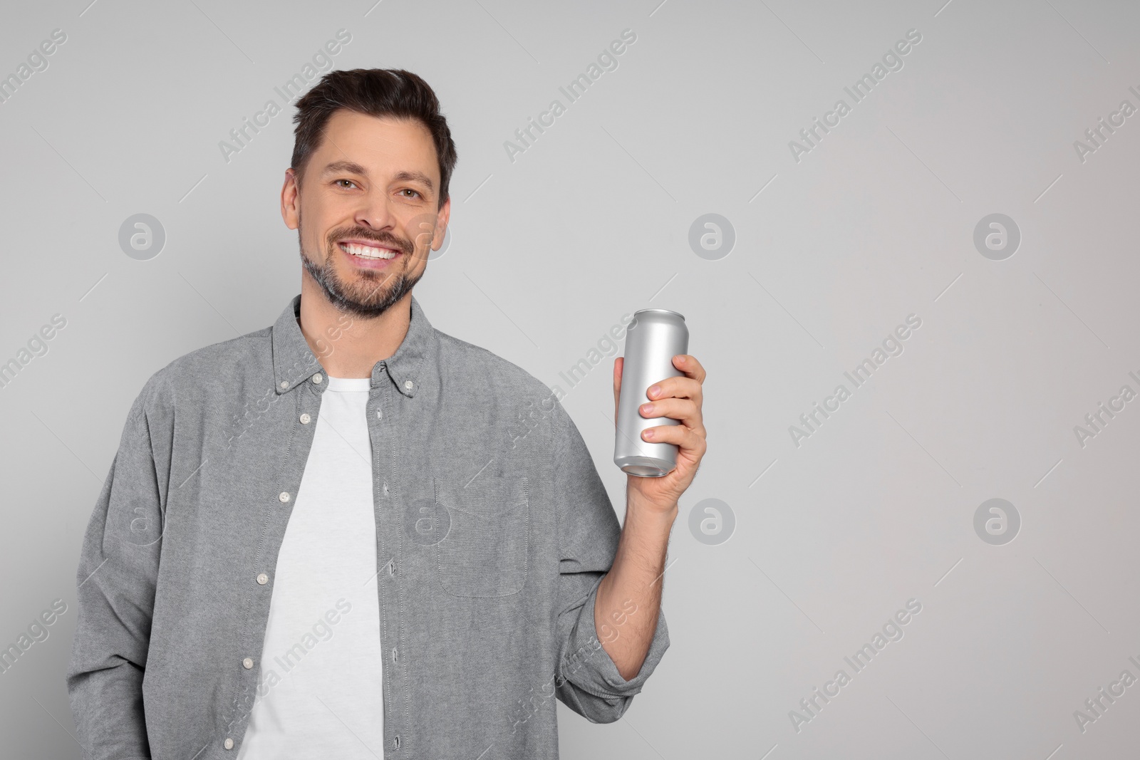 Photo of Happy man holding tin can with beverage on light grey background. Space for text