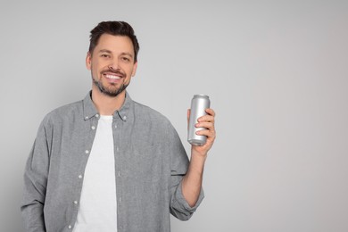 Happy man holding tin can with beverage on light grey background. Space for text