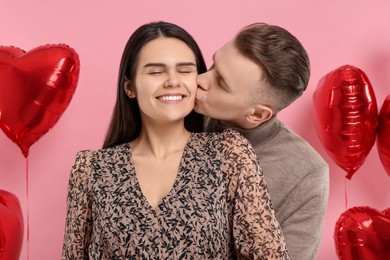Photo of Boyfriend kissing his girlfriend on pink background. Valentine's day celebration