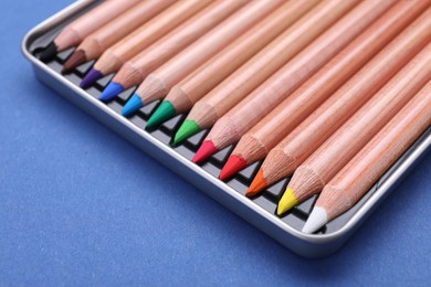 Photo of Colorful pastel pencils in box on blue background, closeup. Drawing supplies