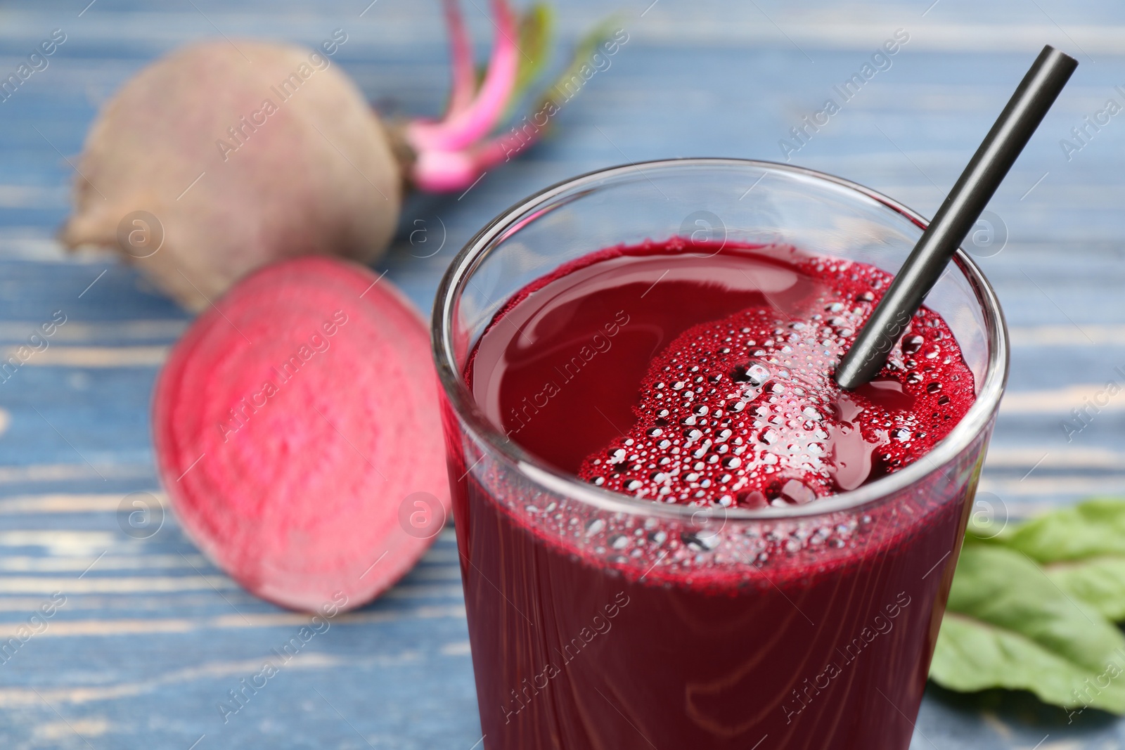 Photo of Freshly made beet juice in glass on blue table, closeup