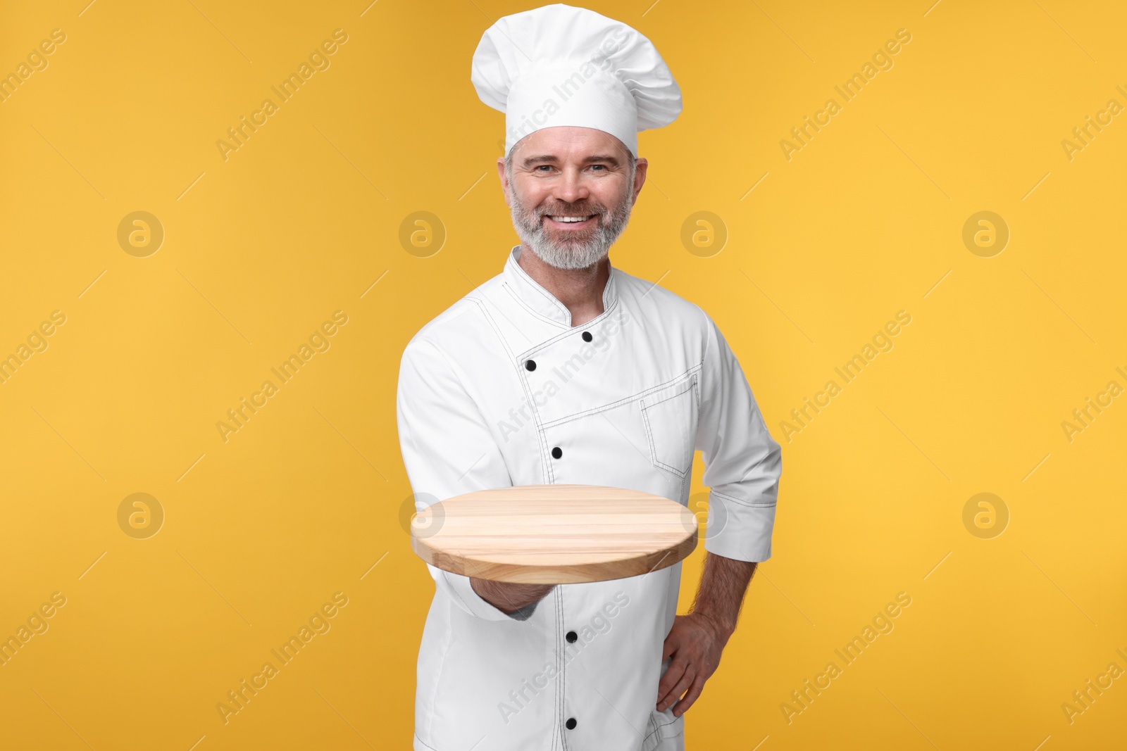 Photo of Happy chef in uniform with wooden board on orange background