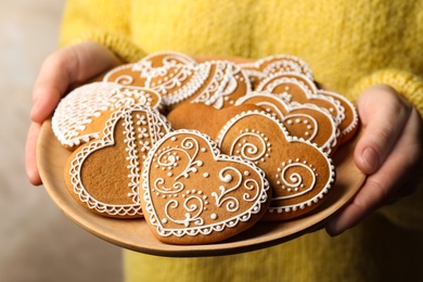 Photo of Woman holding plate with tasty heart shaped gingerbread cookies, closeup