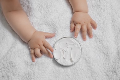 Photo of Cute little baby playing with jar of moisturizing cream on towel, closeup
