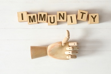 Photo of Cubes with word Immunity and mannequin hand showing thumb up gesture on white wooden table, flat lay