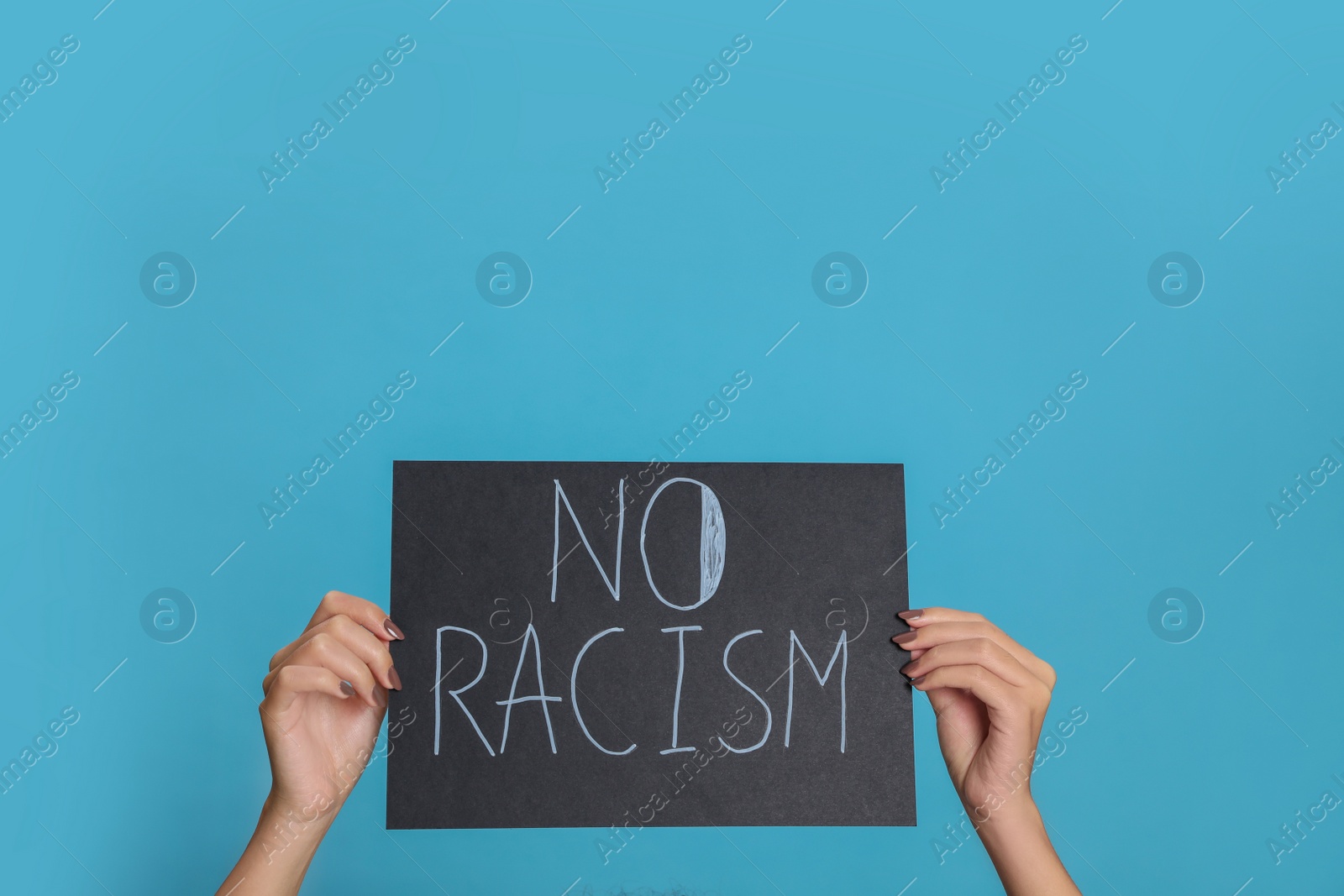 Photo of Woman holding sign with phrase No Racism on light blue background, closeup