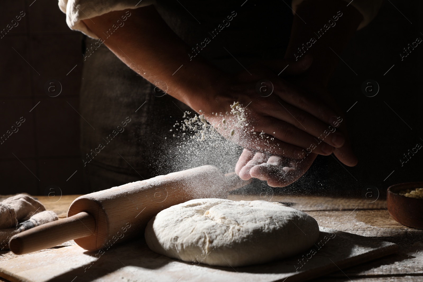 Photo of Man sprinkling flour over dough at wooden table, closeup