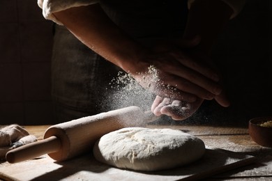 Photo of Man sprinkling flour over dough at wooden table, closeup