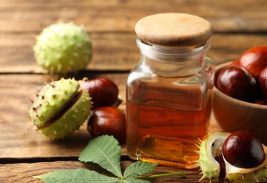 Photo of Chestnuts and jar of essential oil on wooden table