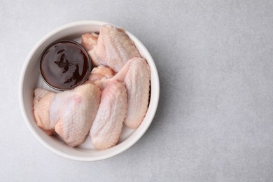 Photo of Plate with marinade and raw chicken wings on light textured table, top view. Space for text