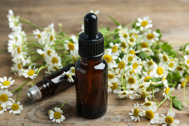 Photo of Bottles of essential oil and fresh chamomiles on wooden table