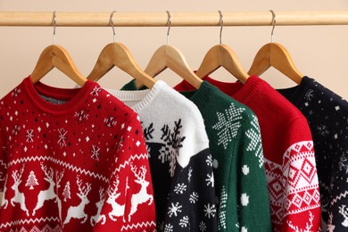 Rack with different Christmas sweaters on beige background