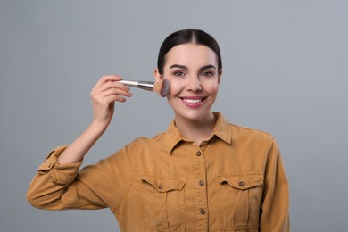 Photo of Happy woman applying makeup on light grey background