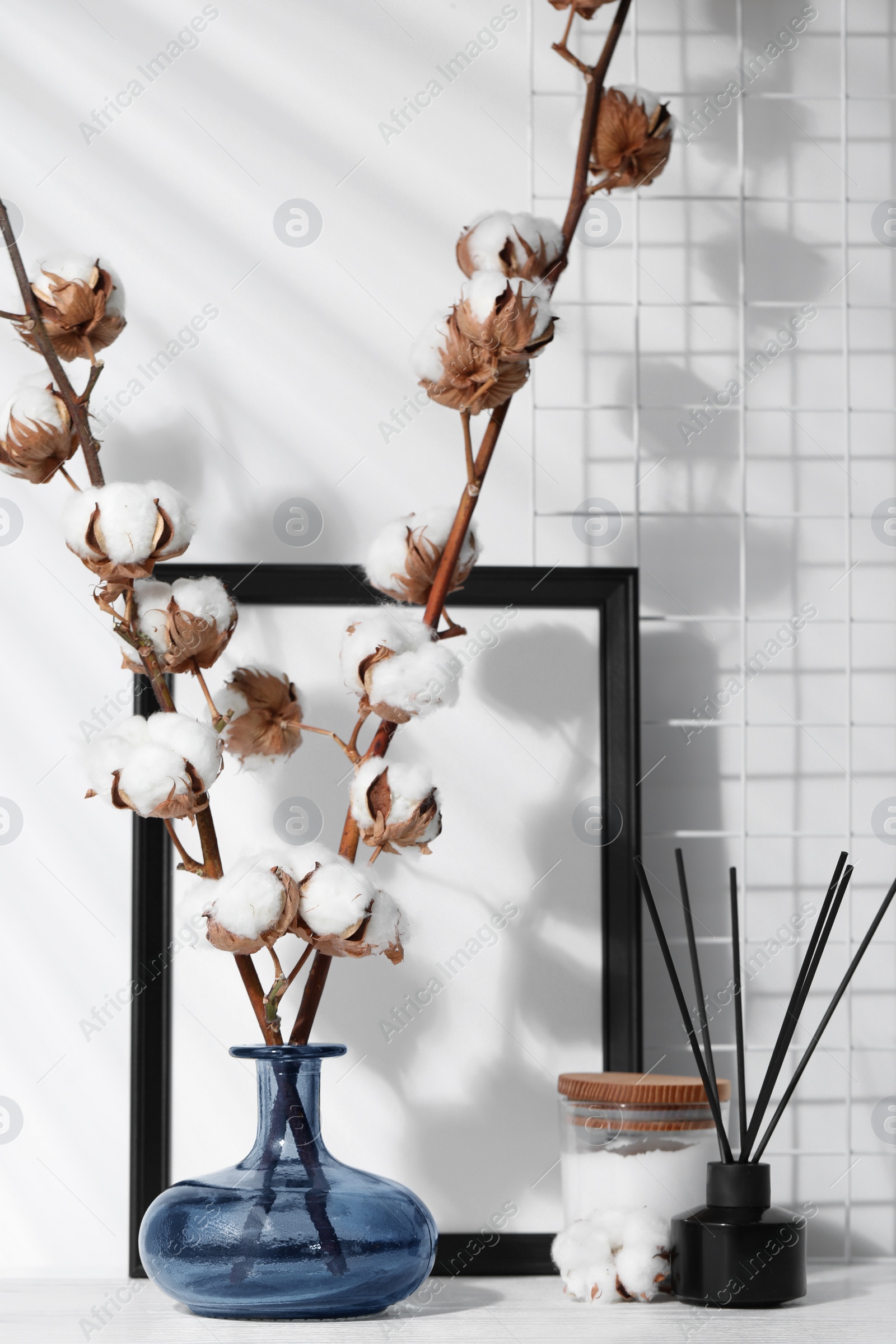 Photo of Reed diffuser, candle and cotton branches with fluffy flowers on white wooden table indoors